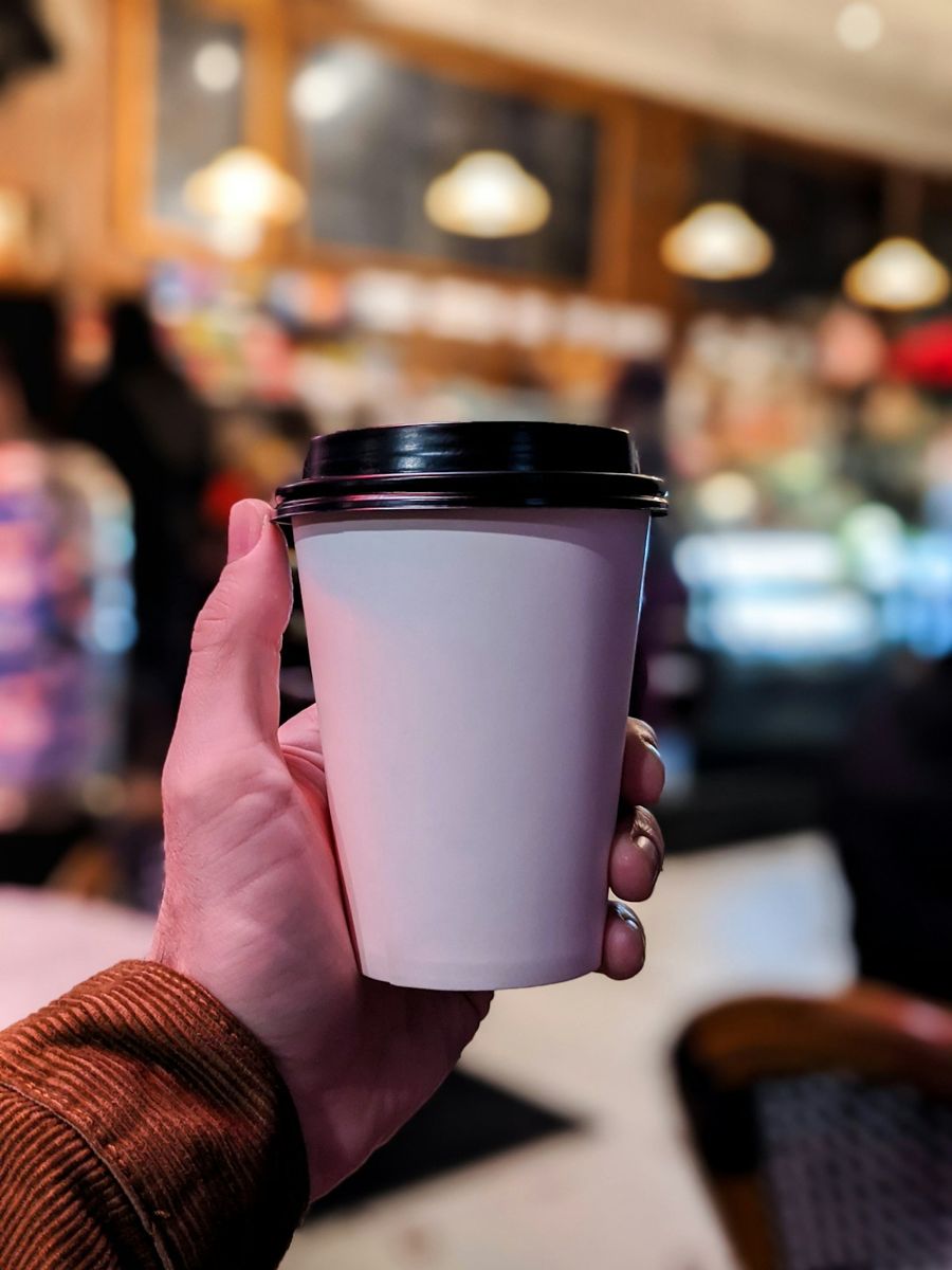 Hand holding a takeaway coffee in a cafe