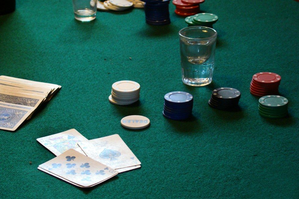 A green-felt table holds neatly stacked red, blue, white, and green poker chips alongside fanned playing cards, including an eight of clubs and an ace of spades.