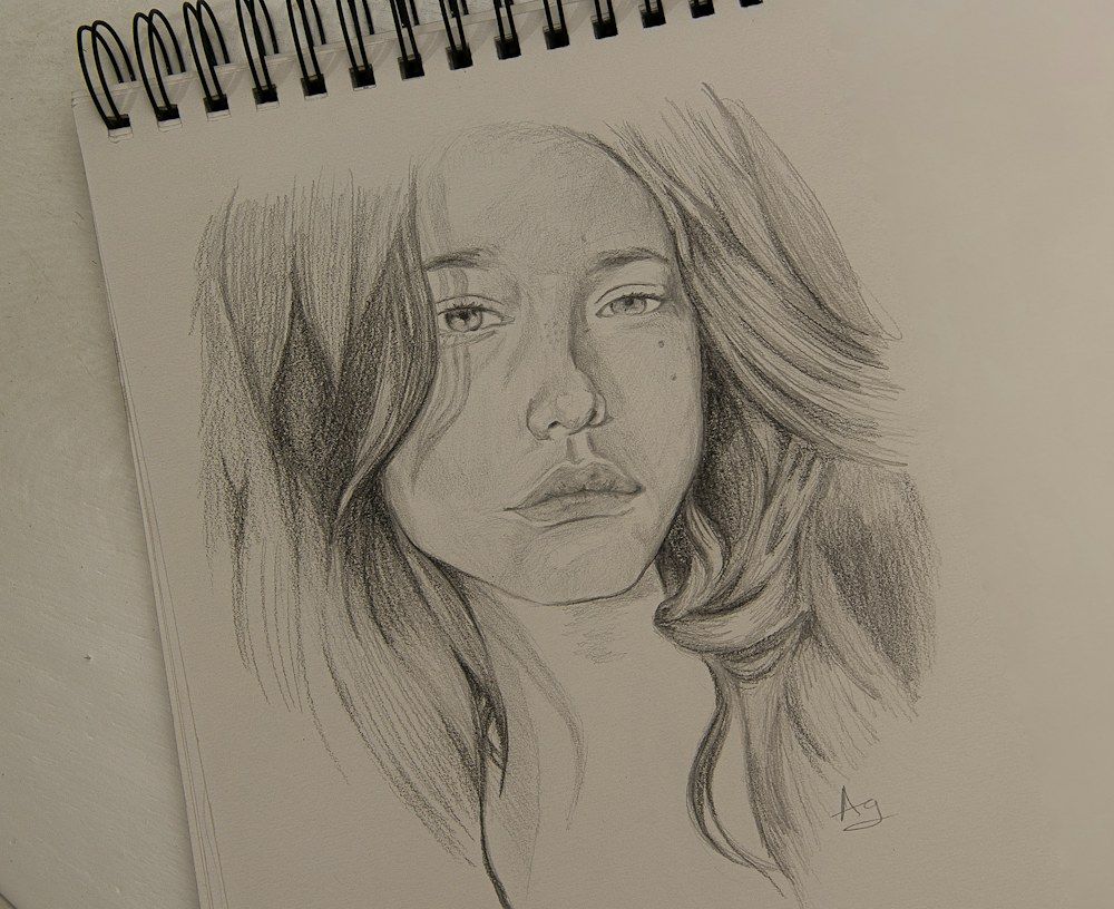 A finely detailed pencil drawing presents a young woman’s face on a clean white sheet of paper.