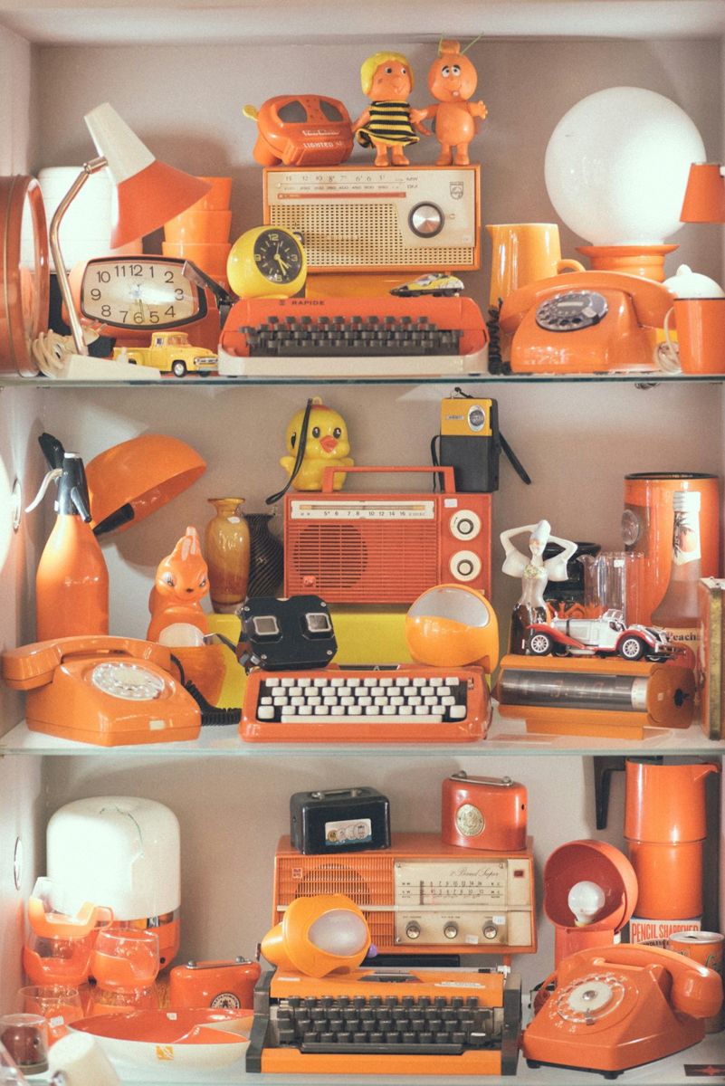 A curated assortment of mid-century orange gadgets and decor items is showcased on glass shelving.