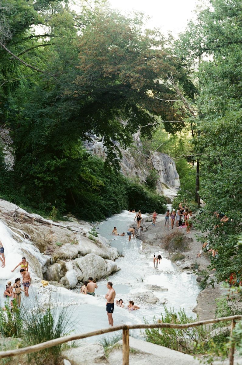 People bathing beside white travertine cascades at Bagni San Filippo in Tuscany.
