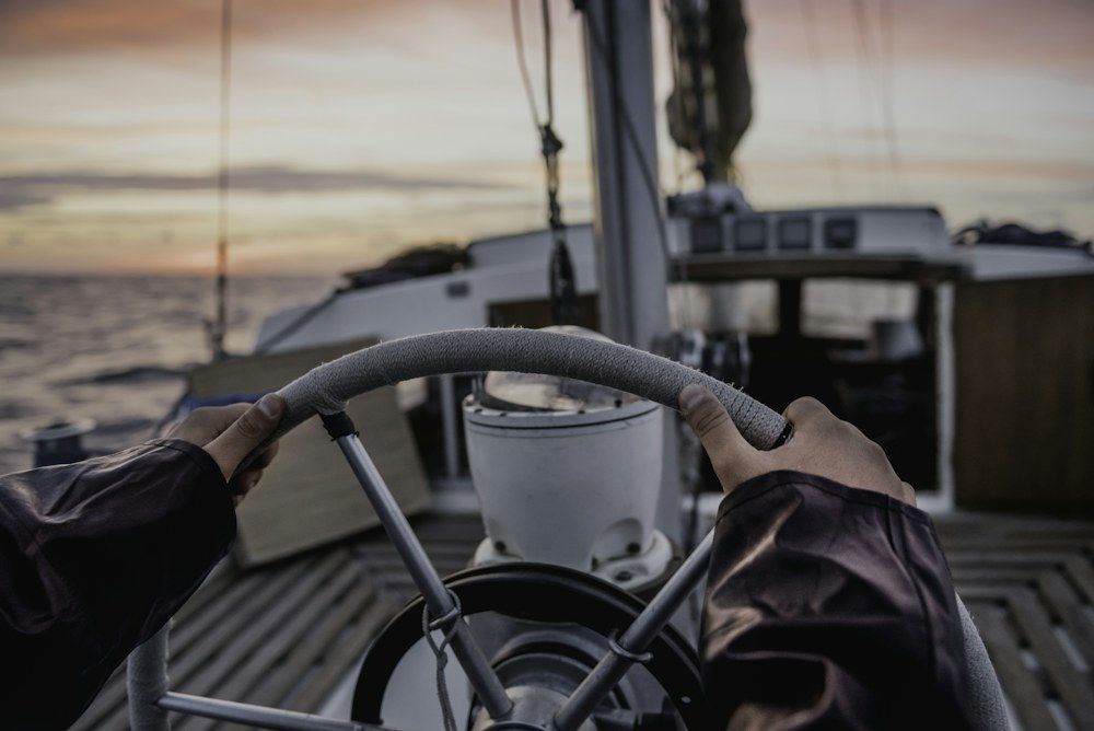 Hands gripping a boat's steering wheel at sunset