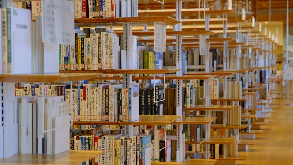 A serene library interior showcases long rows of brown wooden shelves densely packed with books of various sizes and colors.
