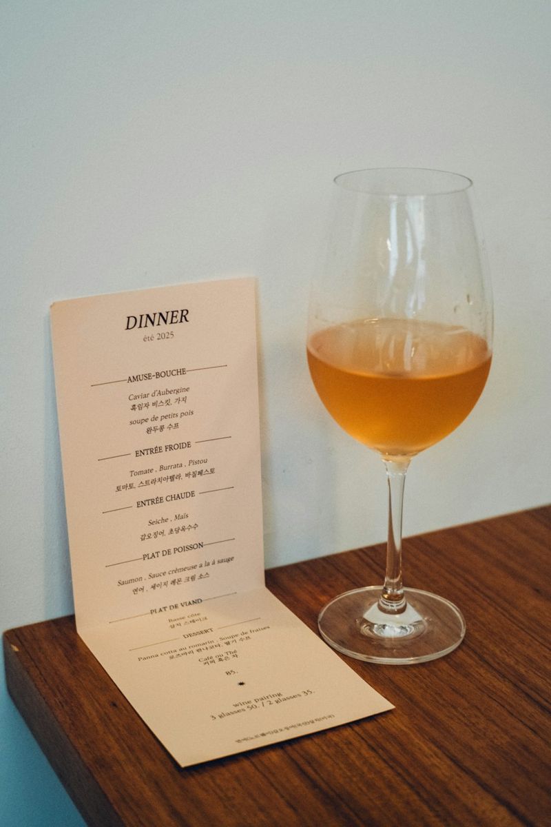 A glass of amber liquid next to a dinner menu.