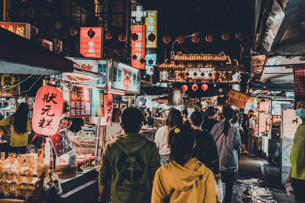 A bustling urban market hall brims with activity as shoppers navigate narrow aisles lined with food stalls.