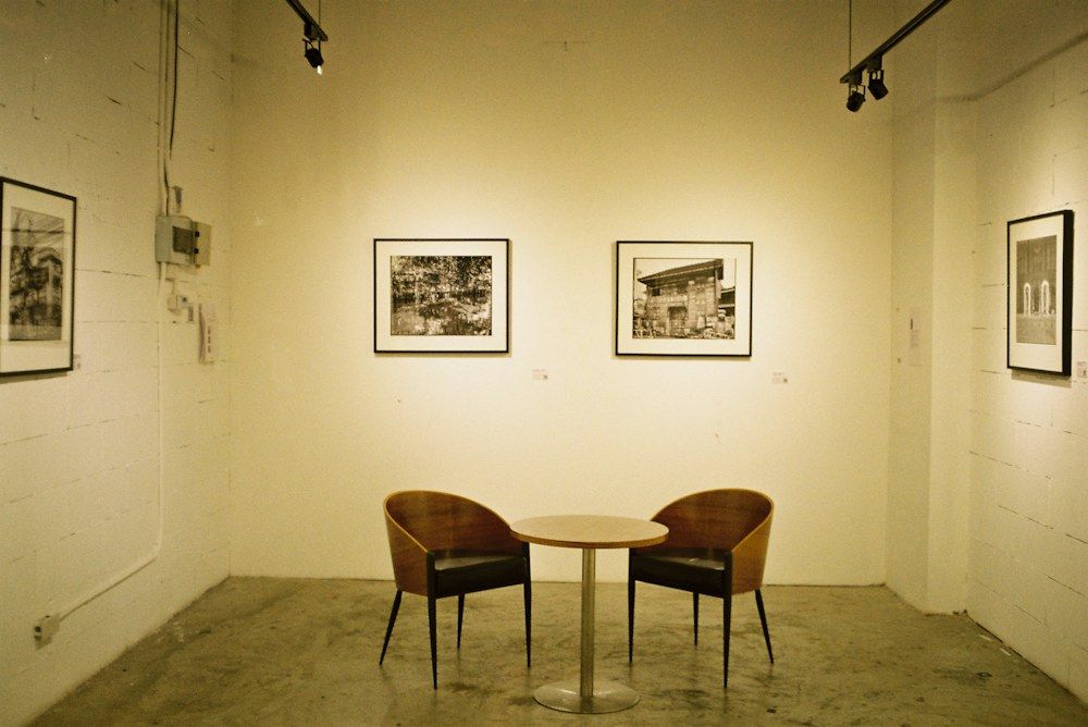 A small exhibition area showcases three framed black-and-white photographs mounted on a stark white wall, illuminated by overhead track lights.