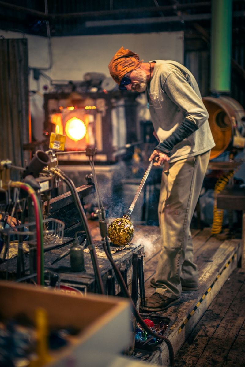 Glassblower shaping molten glass at a workshop furnace