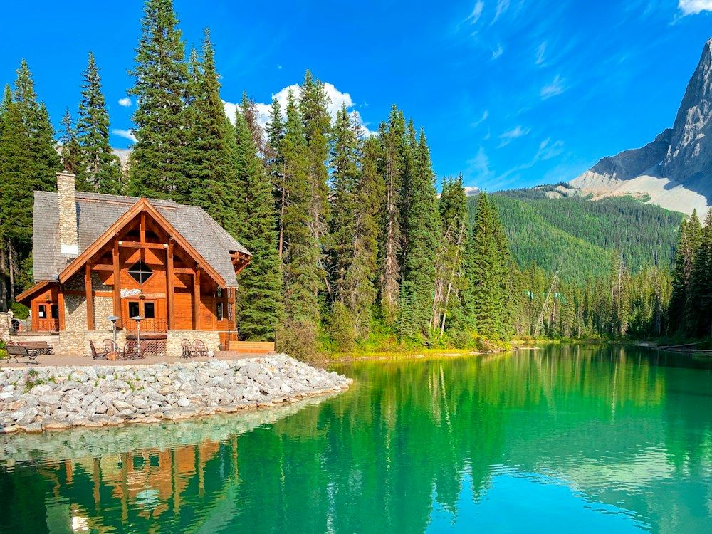 A cabin sits on the shore of a mountain lake