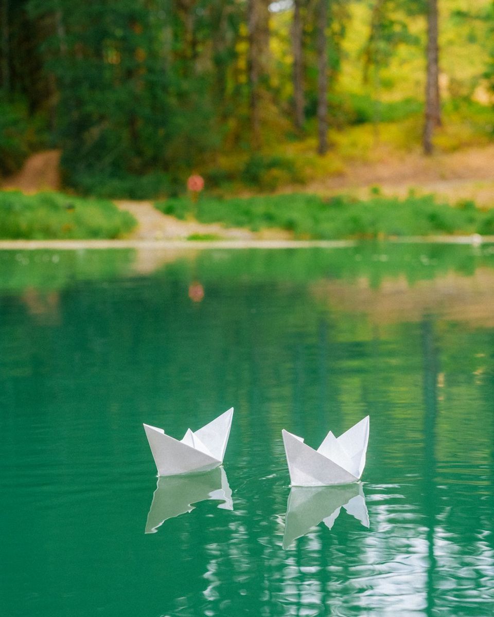 Two folded paper boats floating on green water