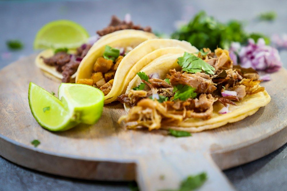A wooden plate topped with three tacos and a lime
