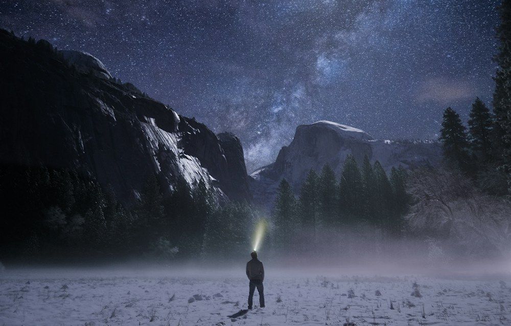 Person wearing a headlamp below mountains at night