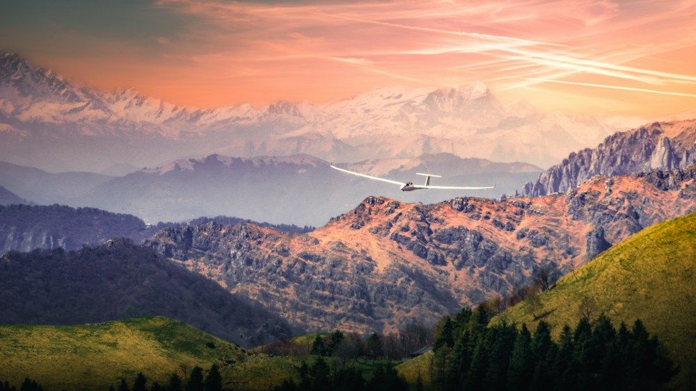 Glider soars over mountains at sunset