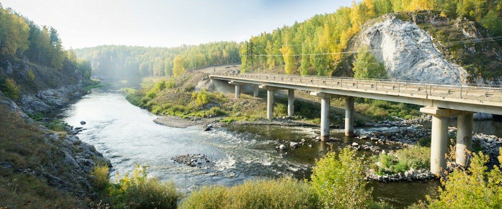 A gray concrete bridge stretches across a calm river, its pillars firmly planted in the water below.