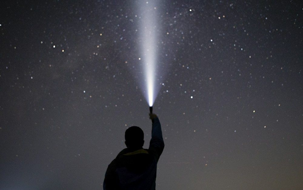 Person shining a flashlight into the night sky