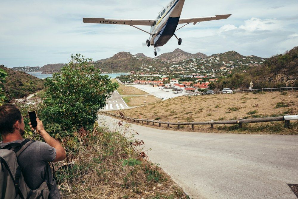 Small propeller aircraft landing on Saint Barthélemy island runway beside a coastal bay