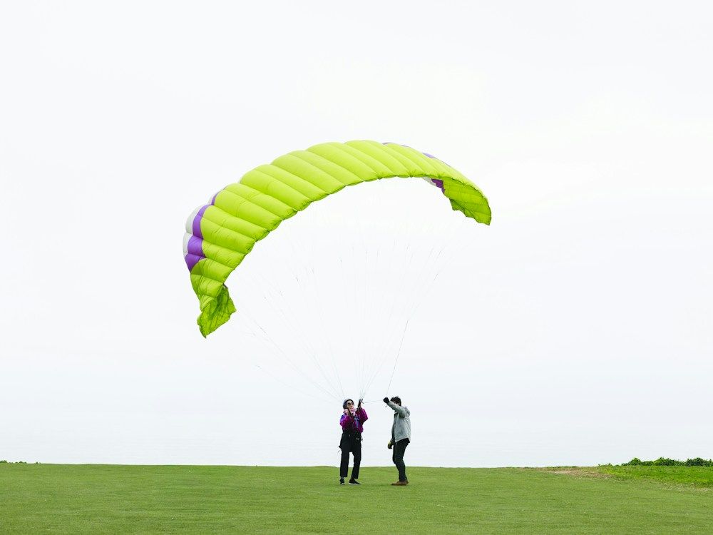 Two people prepare to paraglide on a grassy field.