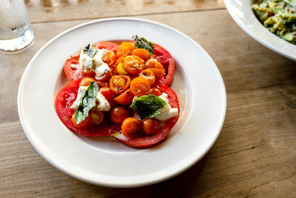 Sliced tomato and green leaf vegetable on white ceramic plate