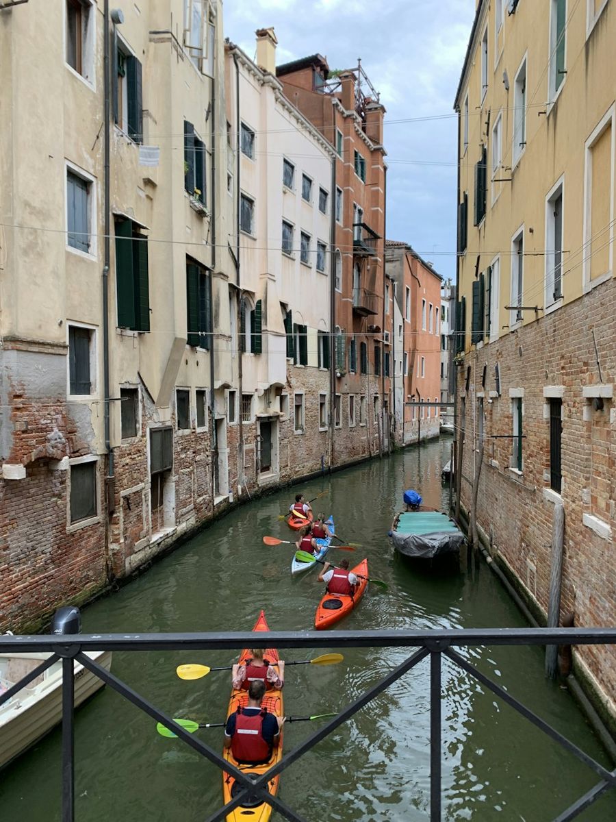A line of brightly colored kayaks glides through a slender waterway nestled between centuries-old Venetian buildings.