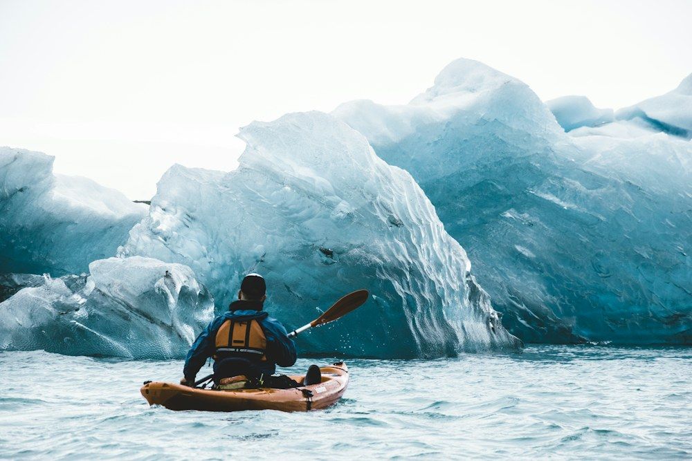 A solitary kayaker navigates the serene, icy waters of Jökulsárlón, Iceland’s famous glacial lagoon.