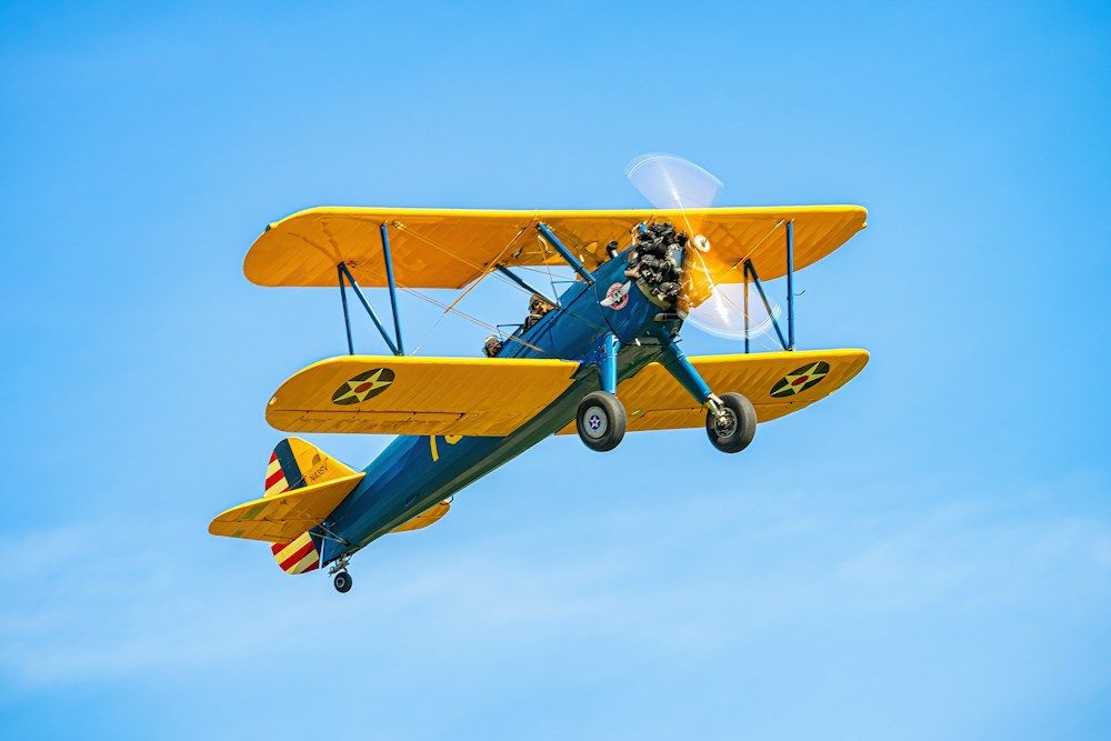 A vintage biplane soars through the bright blue sky.