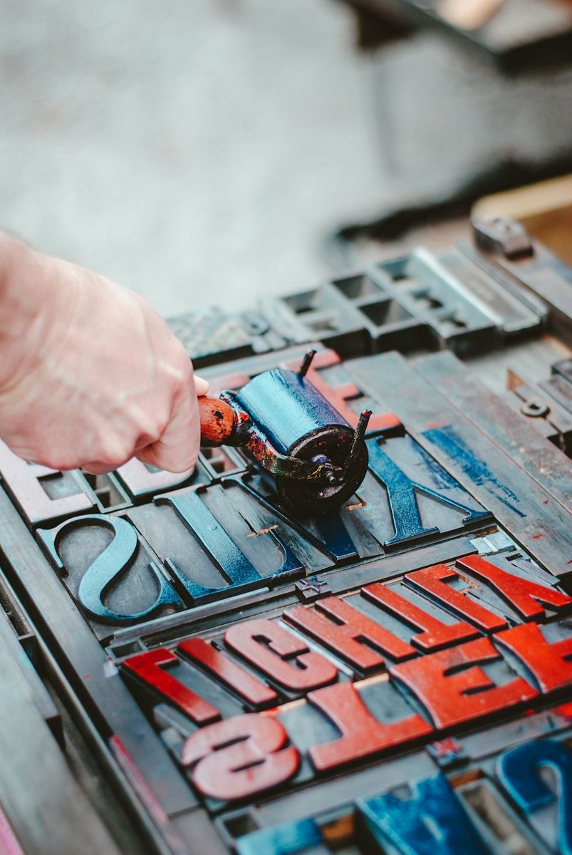 A photographer captured a detailed view of a hand holding a blue ink roller tool above neatly arranged metal type blocks.