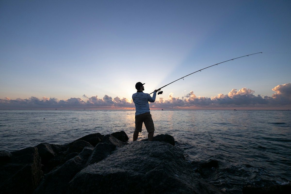 Angler casting from rocks at sunrise