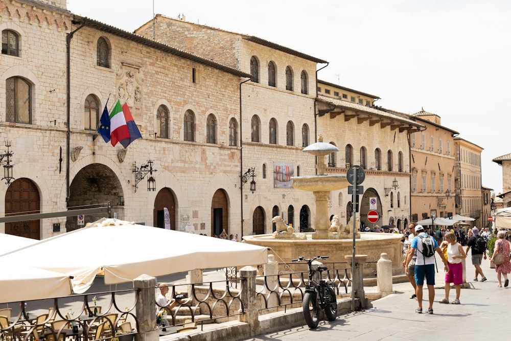 Historic town square with buildings, fountain, and people.
