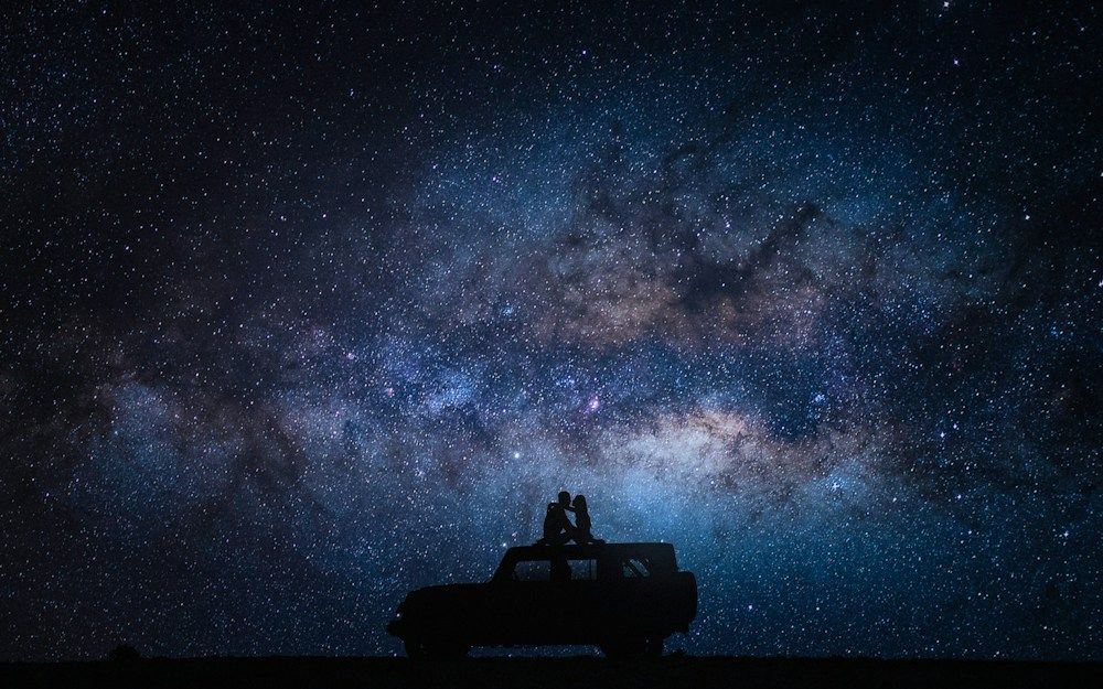 Two people sitting on a truck under the Milky Way